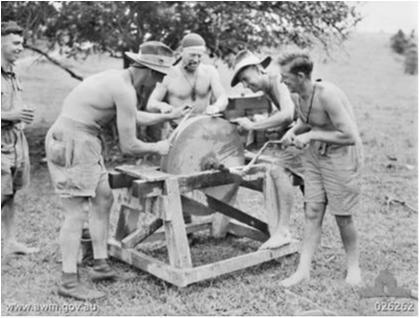 MEN OF THE 2/14TH AUSTRALIAN INFANTRY BATTALION SHARPEN THEIR BAYONETS ON A GRINDSTONE THEY HAD DISCOVERED IN A PLANTATION PADDOCK.