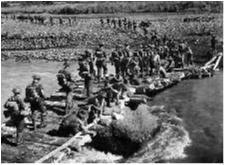 Australian troops cross the Gusap River, a fast-flowing tributary of the Ramu River, during the advance up the valleys, October 1943. Sappers of the 2/5th Field Company, Royal Australian Engineers, were still completing the bridge.