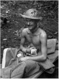Private Keith Kilpatrick, 2/27th Battalion, sits on a stretcher at Dumpu after being wounded in the hand in defence of a feature called John's Knoll on 12 October, 1943. Fragments from the grenade that wounded him also perforated his helmet.